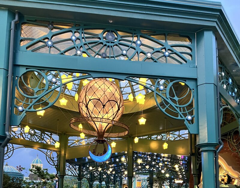 Celestial Park pavilion at dusk: ornamental teal ironwork, celestial motifs, and a balloon chandelier with hanging star lights