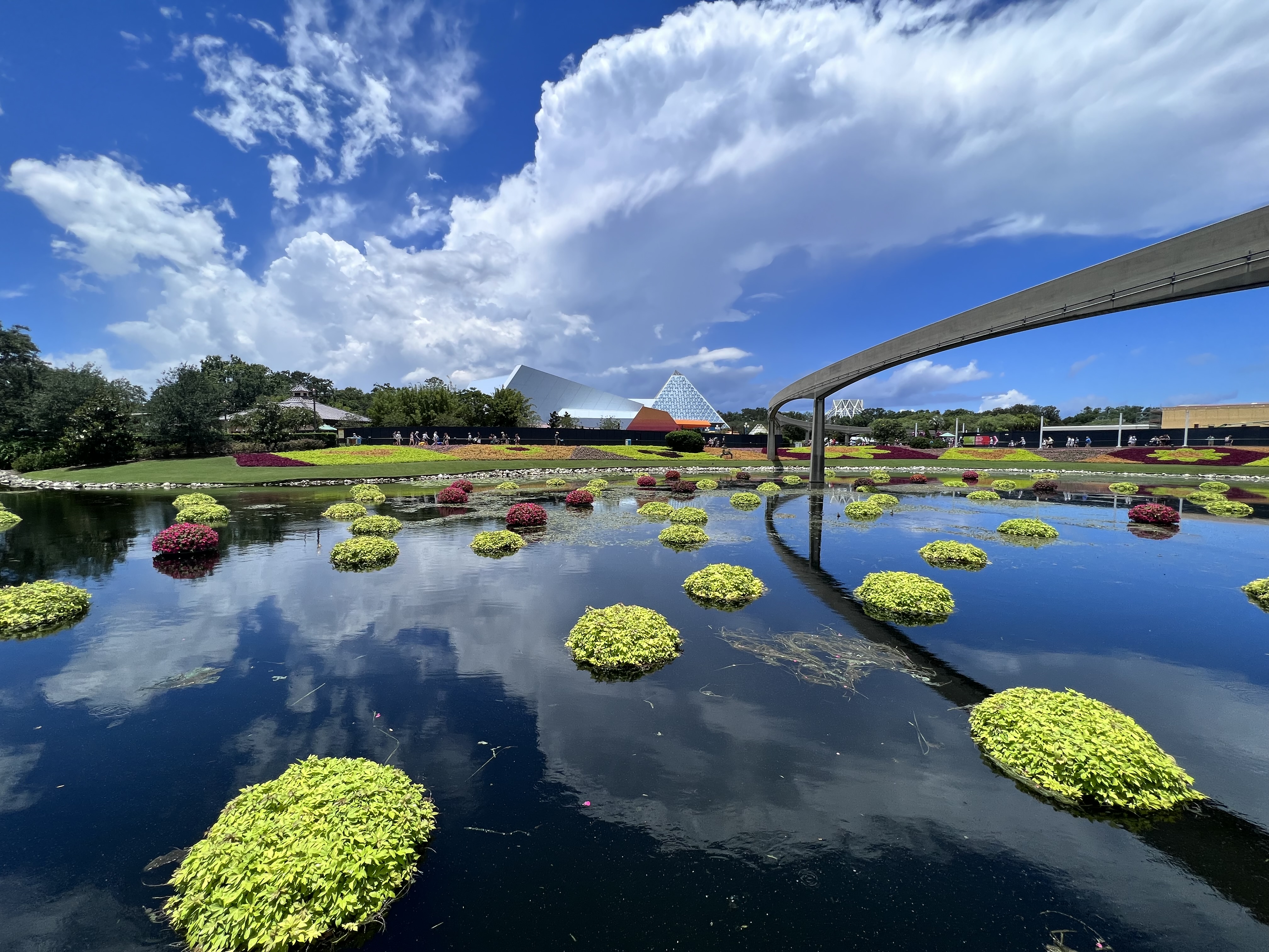 EPCOT Flower and Garden Festival: floating flower islands reflected in the lagoon with the Imagination pavilion and monorail in the background under blue skies.