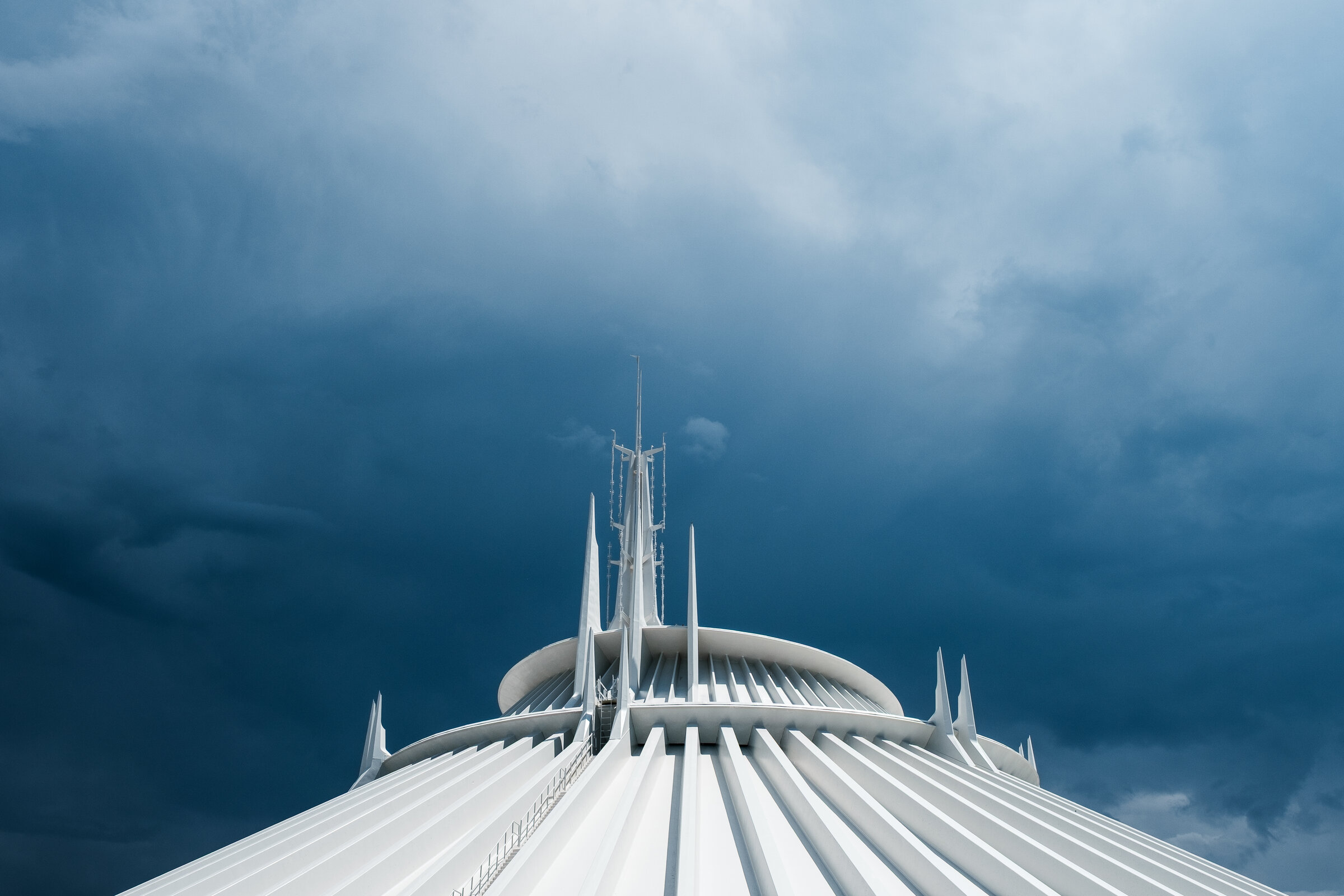 Magic Kingdom's Space Mountain photographed from below: the white conical exterior with radial ribs and a central antenna mast against a moody cloudy sky