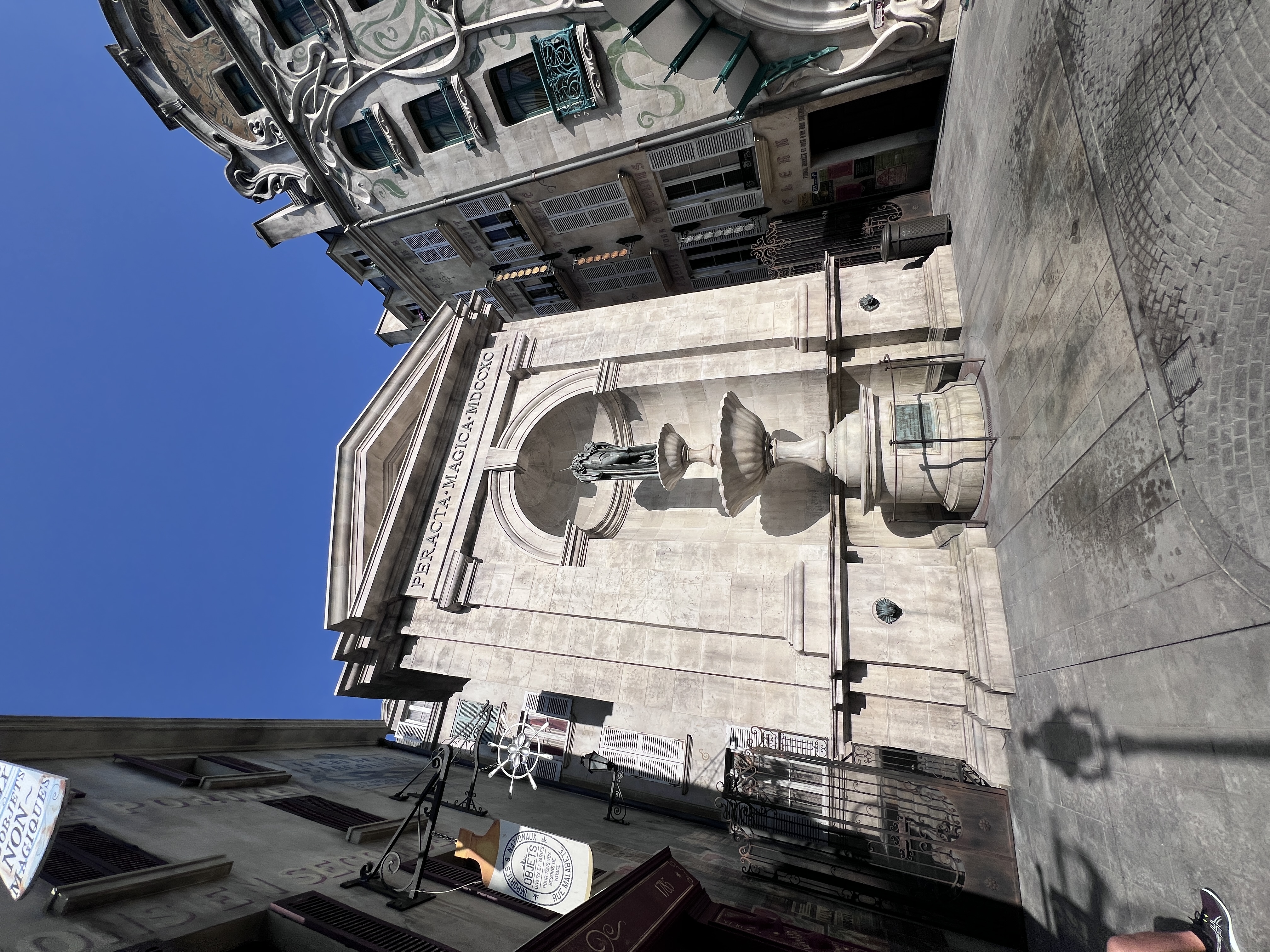 The Ministry of Magic facade rises against a clear blue sky at Universal's Epic Universe, its grand stone archways and ornate fountain dwarfing the guests below